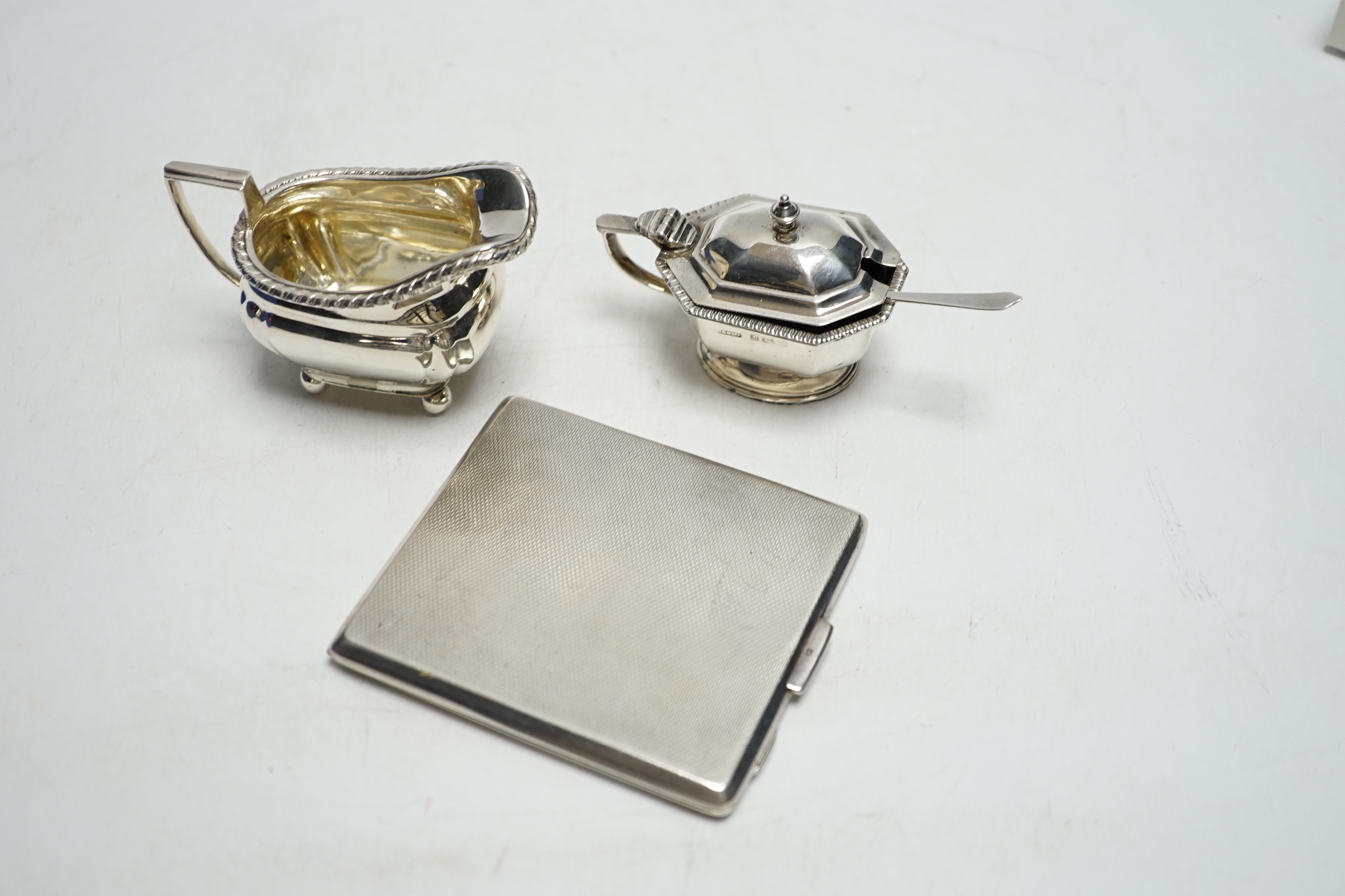 A George VI engine turned silver cigarette case, a silver lidded mustard pot and a small silver cream jug.